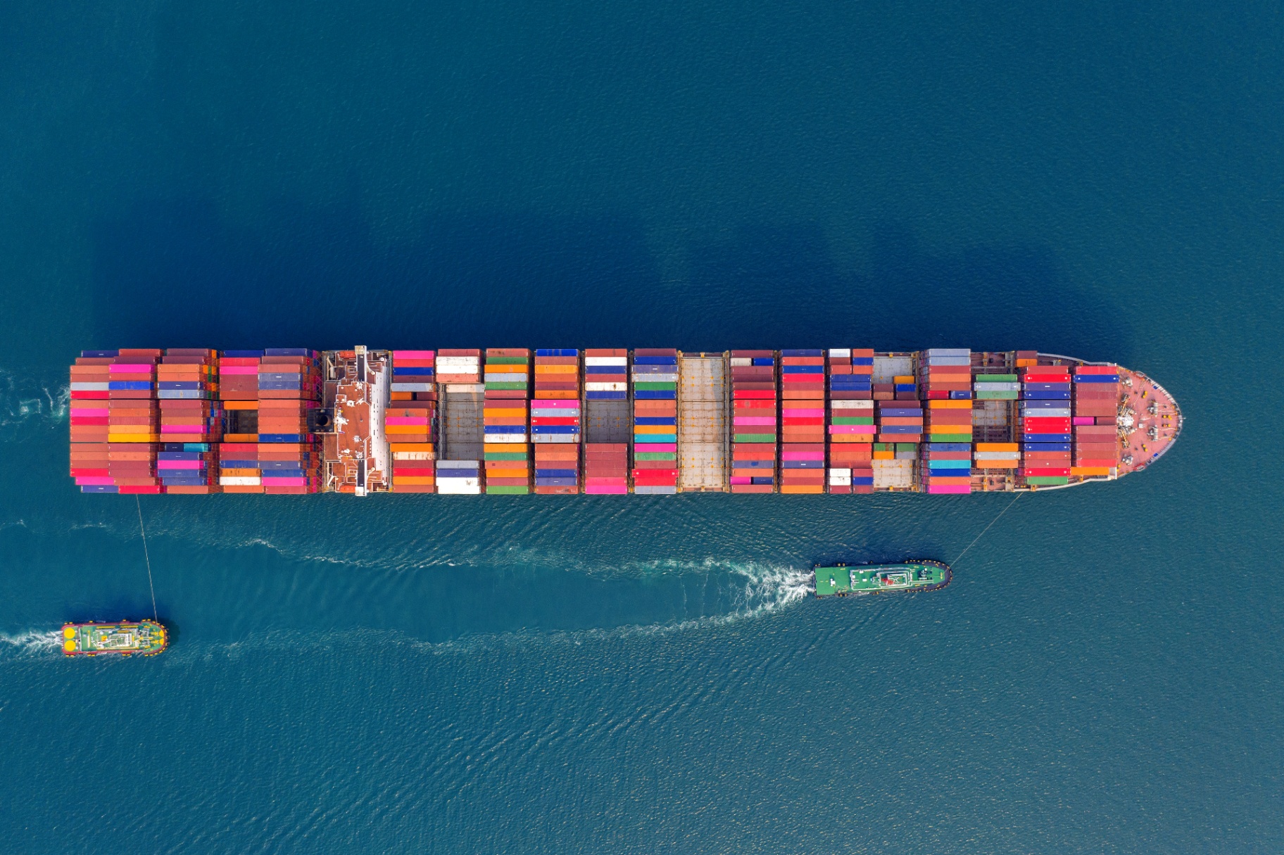 Vista aérea de navio porta-contêineres escoltado por rebocadores em alto-mar